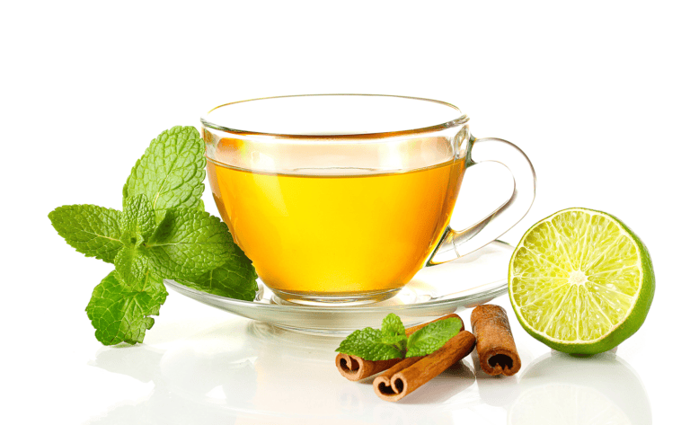 A clear cup of tea with mint leaves, a slice of lime, and cinnamon sticks on a white background.