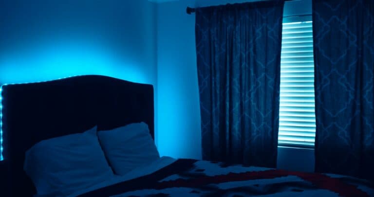 A dimly lit bedroom with blue ambient lighting and a patterned comforter on the bed.