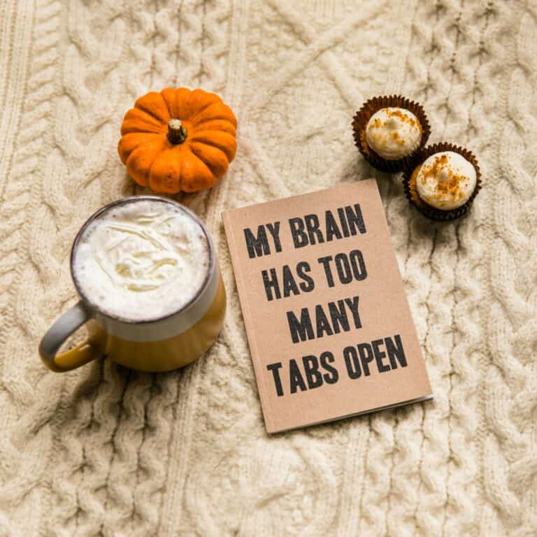 A cozy autumnal setting with a latte, a mini pumpkin, two bite-sized desserts, and a humorous note stating, "my brain has too many tabs open.