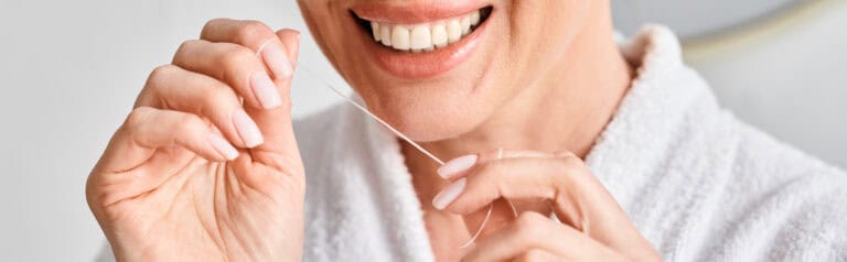 Close-up of a smiling person in a white robe flossing their teeth.